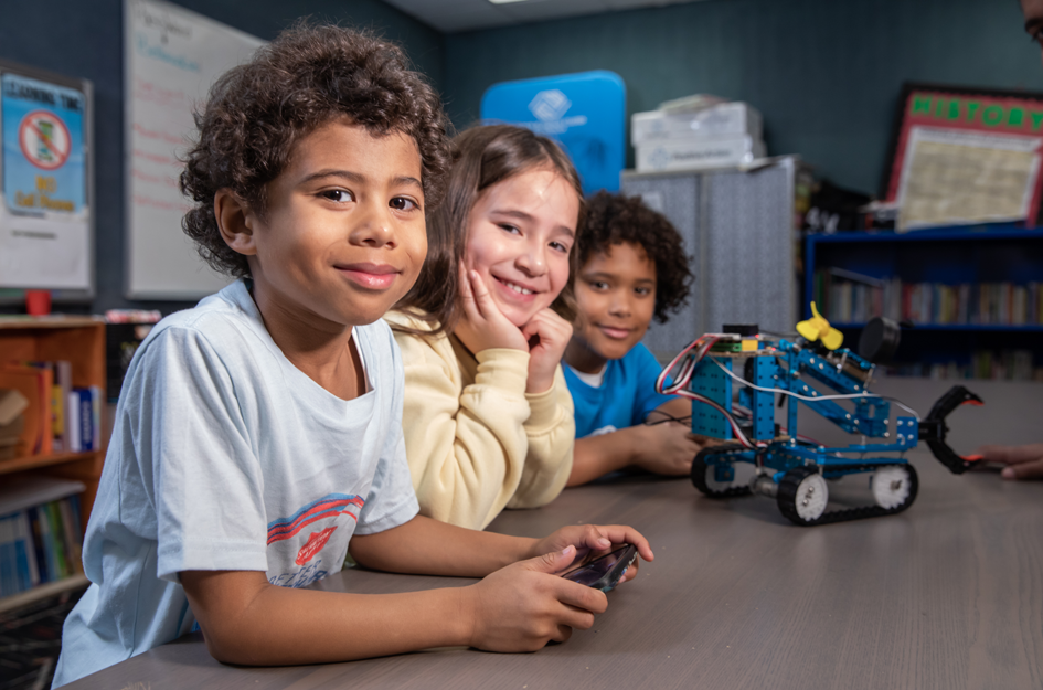 Three Club kids smiling at camera with their robot proudly displayed