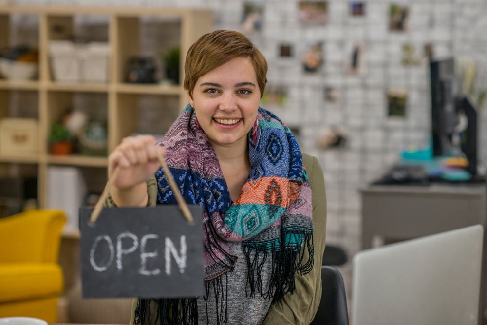Teen girl with store Open sign smiling at camera