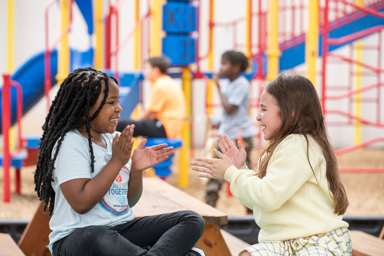 Two adorable Club girls playing patty-cake on the playground