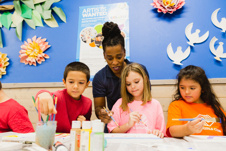 Club kids working on art project with Youth Development Professional style=